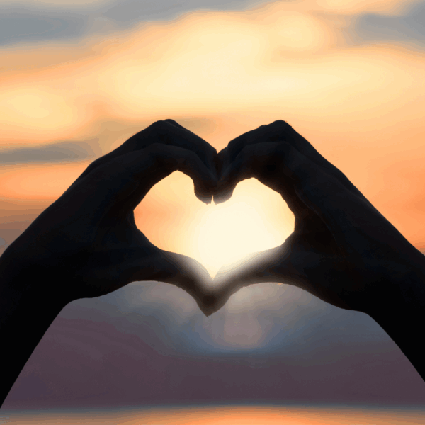 Mains formant un cœur au coucher du soleil symbolisant l'amour de soi du Manifesteur en Design Humain