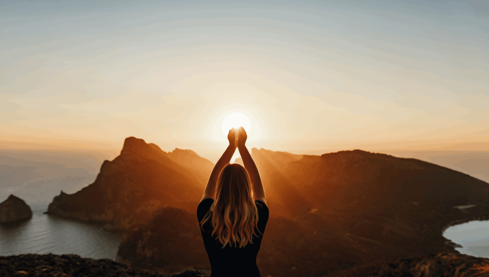 Femme en méditation les bras levés vers le soleil face à un paysage montagneux au coucher du soleil, symbolisant l'alignement énergétique du Design Humain